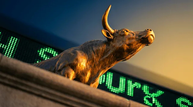 A close-up shot of a classic bronze bull statue gleaming under dramatic golden light, symbolizing the record-breaking rally, with a blurred stock ticker board glowing green in the background.