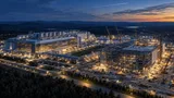 Aerial dusk view of a semiconductor fab campus in upstate New York with one nearly completed building and a second still under construction with cranes, representing twin chip fabs at different project stages.