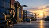 A warehouse loading dock at dawn: a line of steel shipping containers stacked beside an idle forklift, its raised forks catching the first sunlight while a coil of thick industrial cable rests nearby.